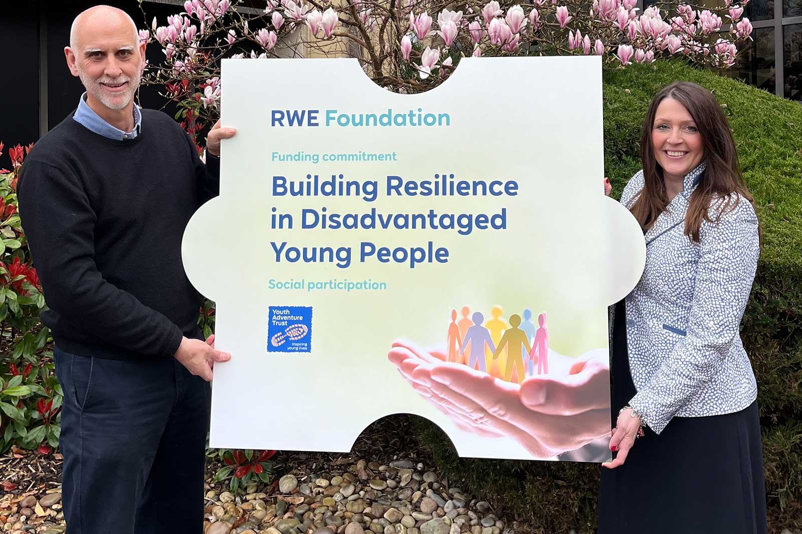 Zwei Personen halten ein Schild, das das Engagement der RWE Foundation zur Stärkung von benachteiligten jungen Menschen bewirbt.