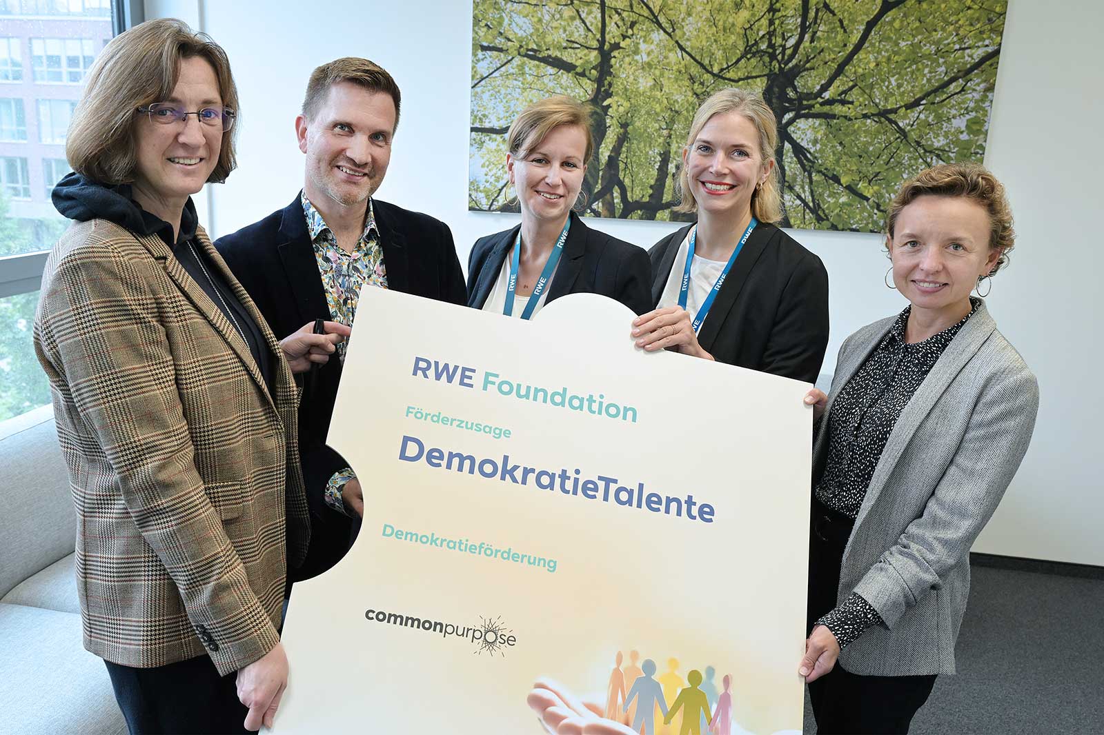 Eine Gruppe von Personen hält ein Schild der RWE Foundation zur Förderung von DemokratieTalenten in einem Innenraum.