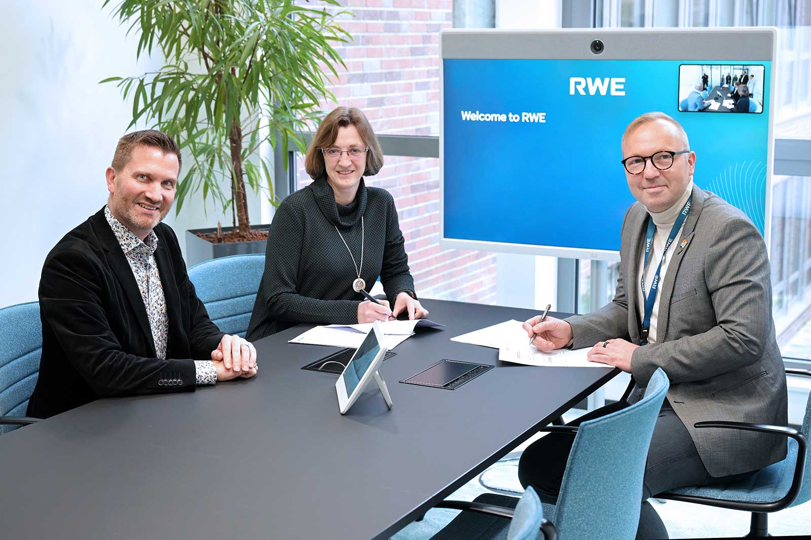 A team meeting at RWE with three participants discussing and taking notes at a modern conference table.