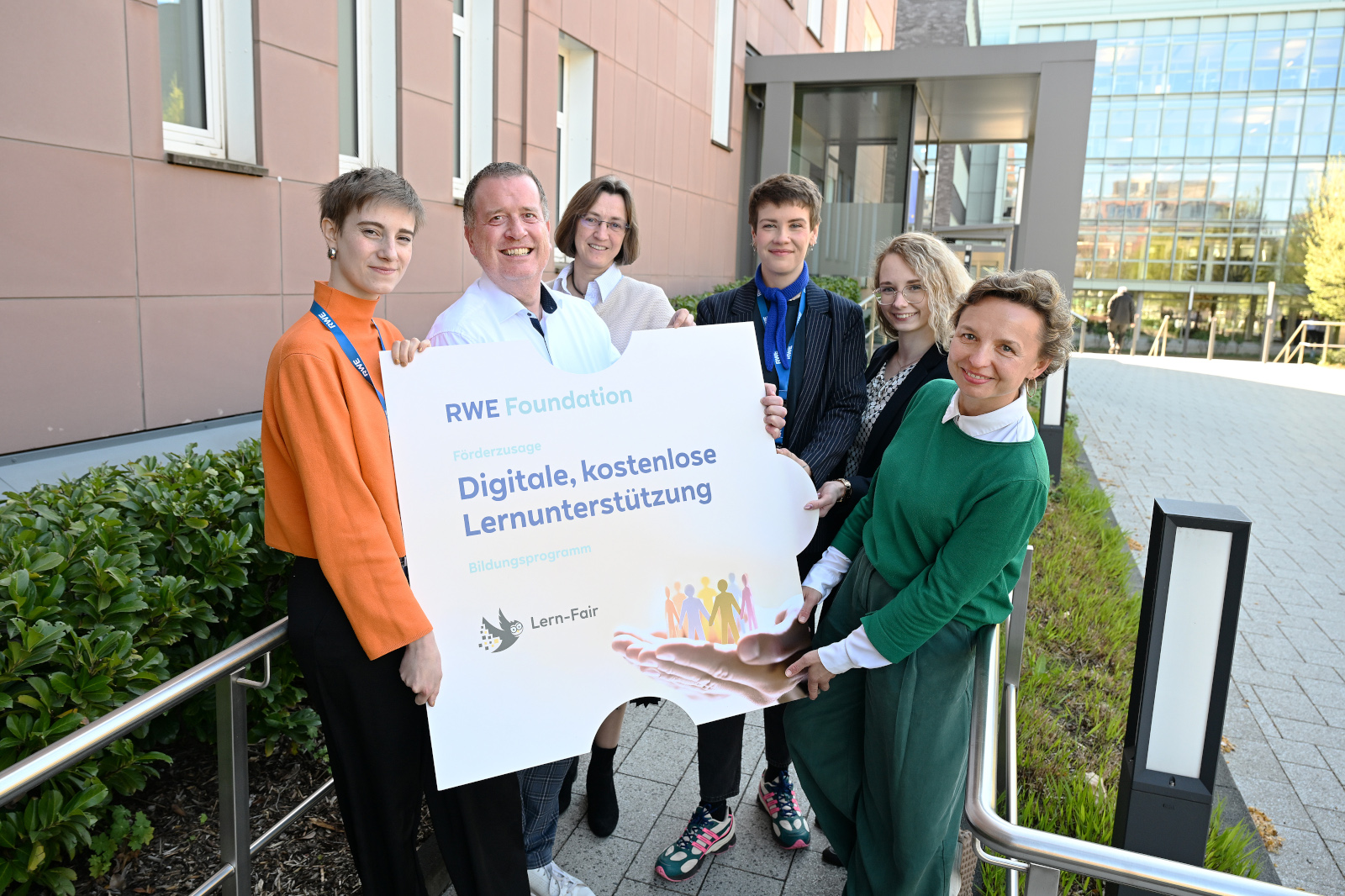 Sechs Personen halten ein Schild mit der Aufschrift 'RWE Foundation' und Informationen zur digitalen Lernunterstützung.