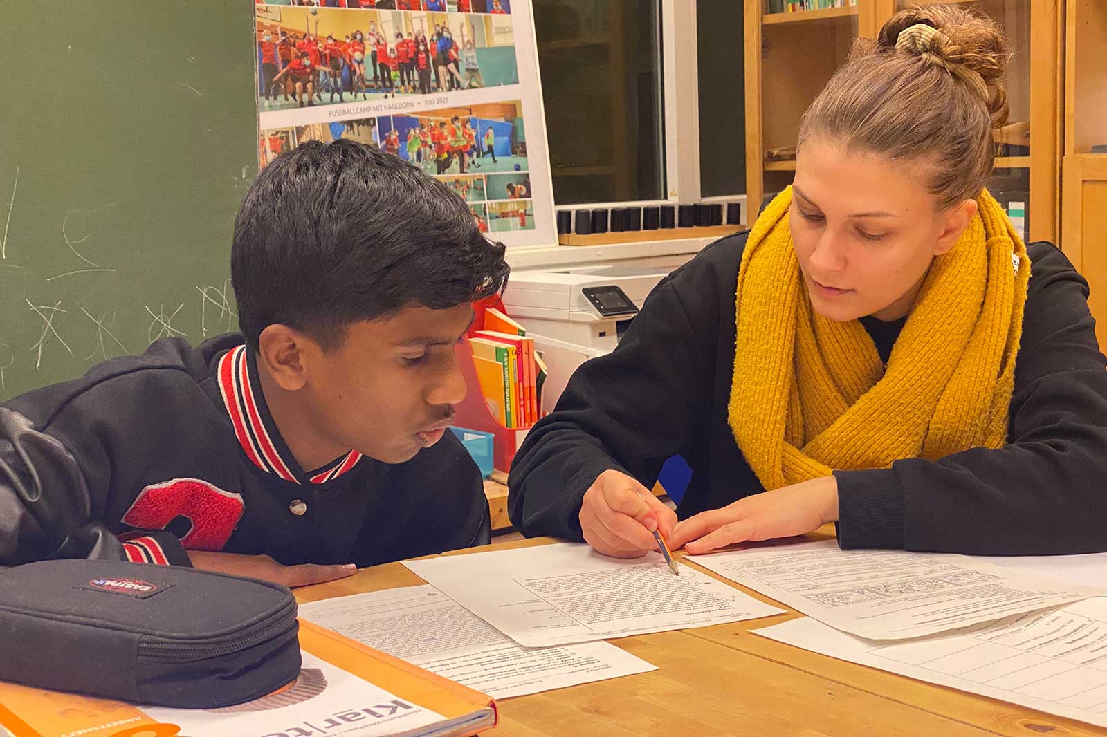 A boy and a girl focus on studying together. They are working on documents at a table surrounded by books.