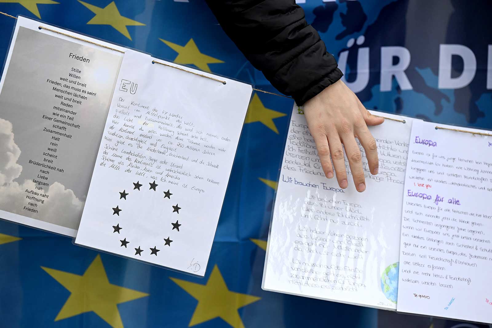 A hand holds a document with writings about Europe, surrounded by EU symbols against the backdrop of an EU flag.