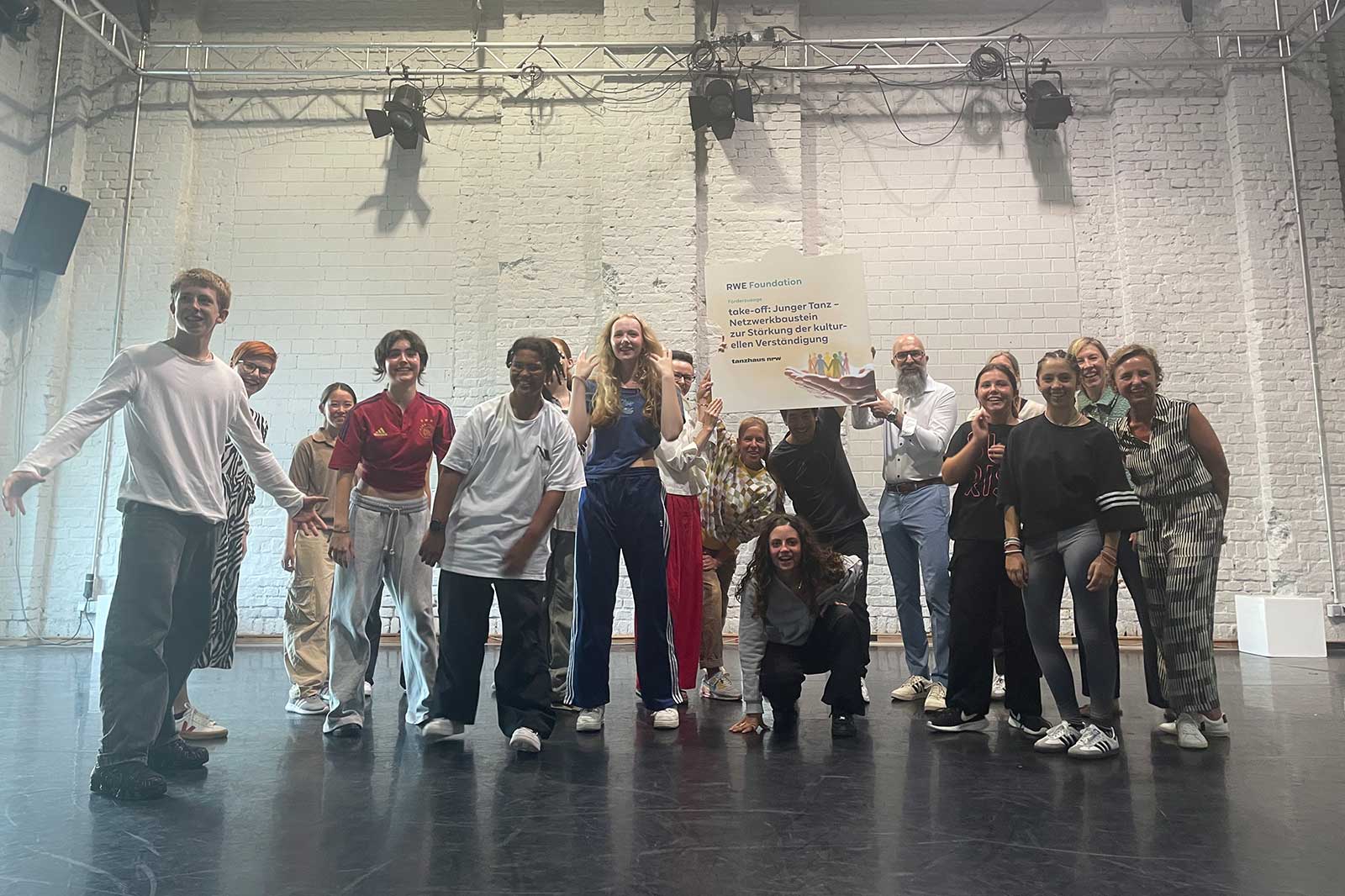 Eine diverse Gruppe von Jugendlichen posiert dynamisch in einem Tanzstudio und zeigt ein unterstützendes Umfeld für Kreativität.
