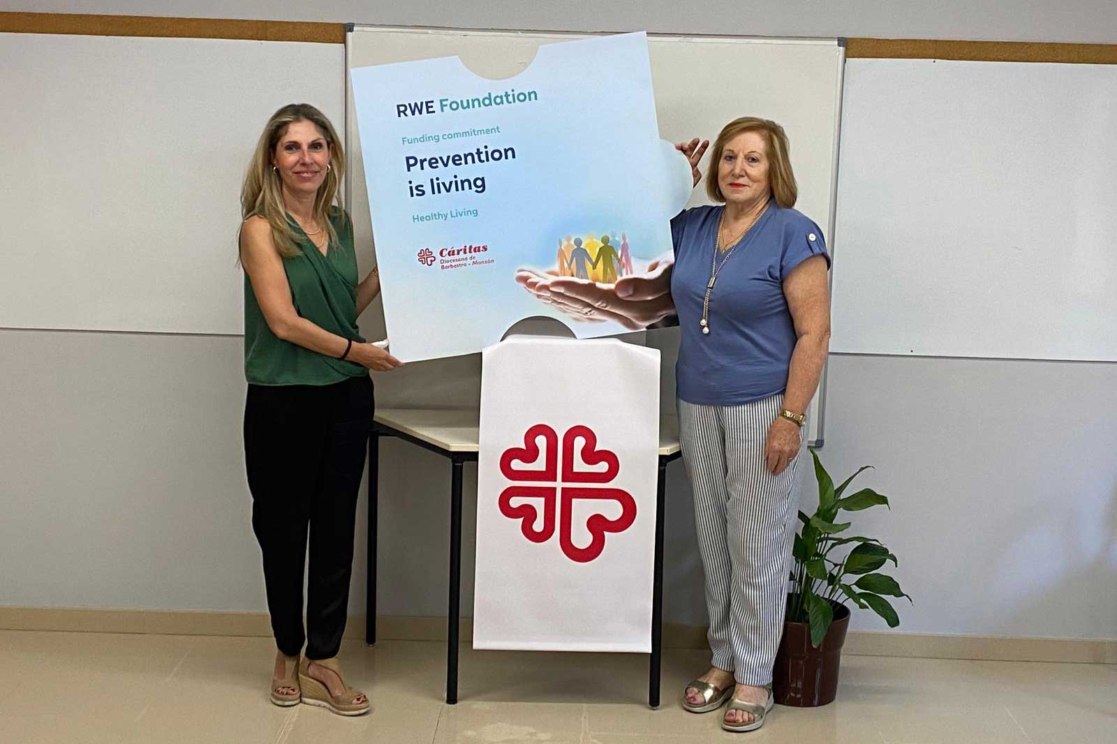 Two women hold up a large sign that reads 'Prevention is living' in front of a plain wall.