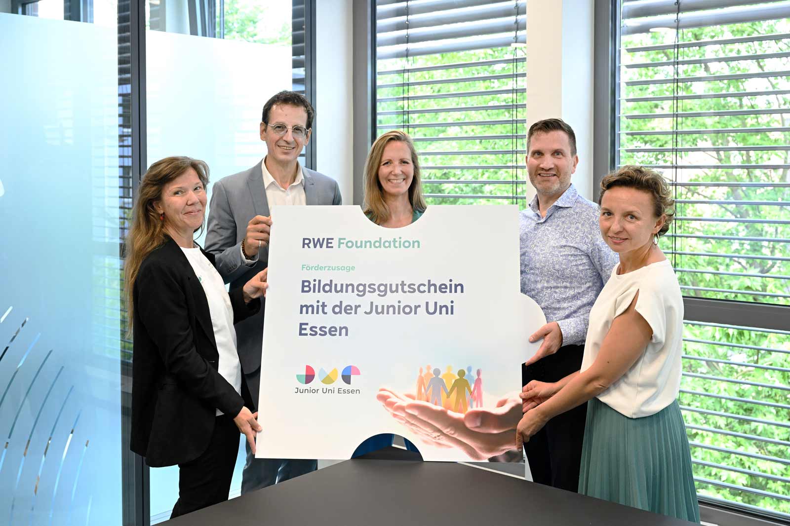 A group of five individuals holds a sign from the RWE Foundation for education vouchers with Junior Uni Essen.