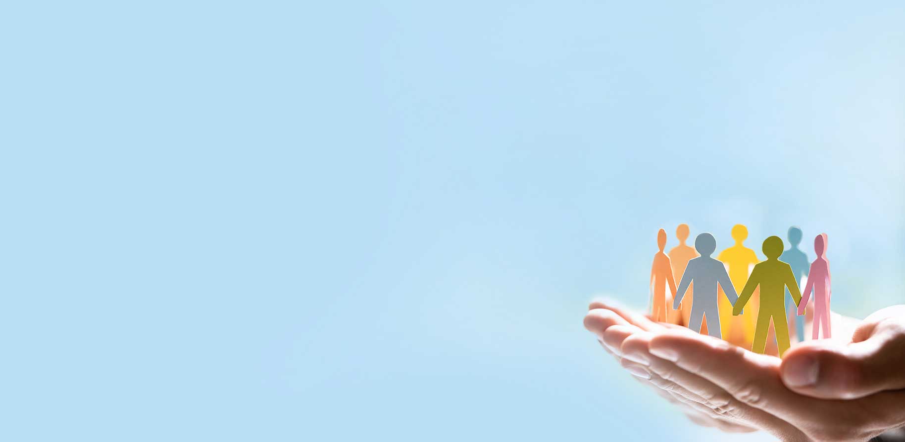 A hand holds colourful paper figures holding hands against a blue background.