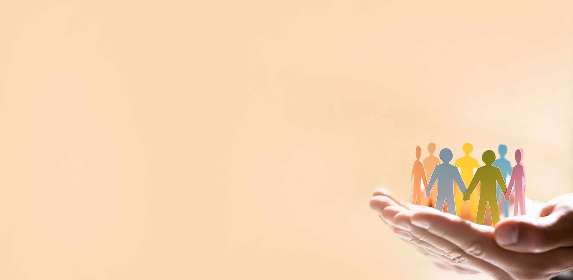 Hände halten eine Gruppe farbiger Papierfiguren, die Händchen haltend angeordnet sind, vor einem hellen Hintergrund.