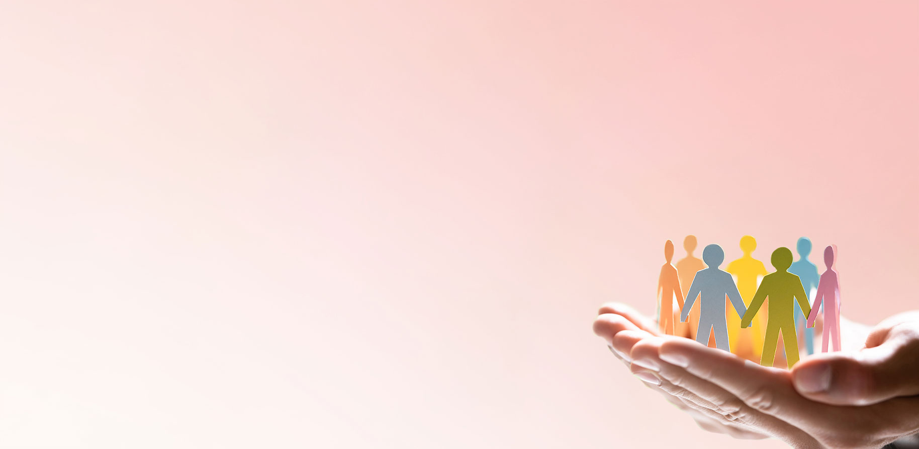 Two hands hold colourful paper figures representing people. The background is softly pink.
