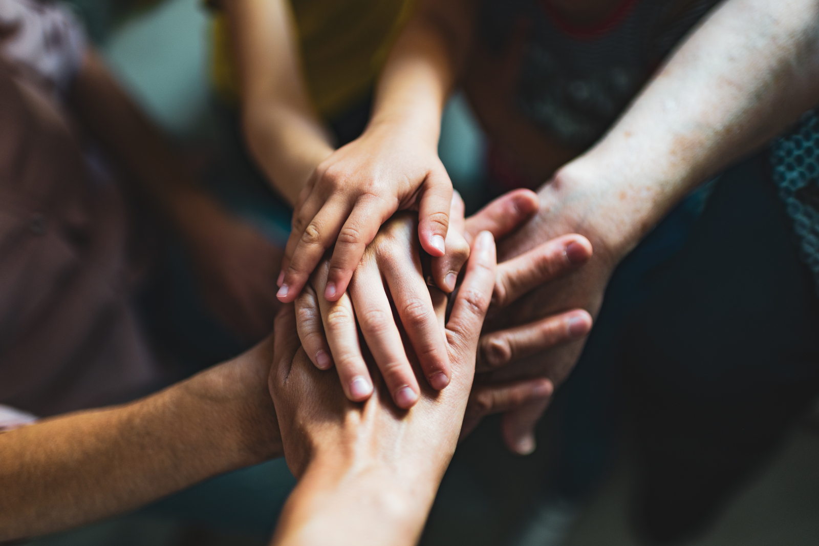 A group of hands, including children's hands, is stacked on top of one another, symbolising community and collaboration.