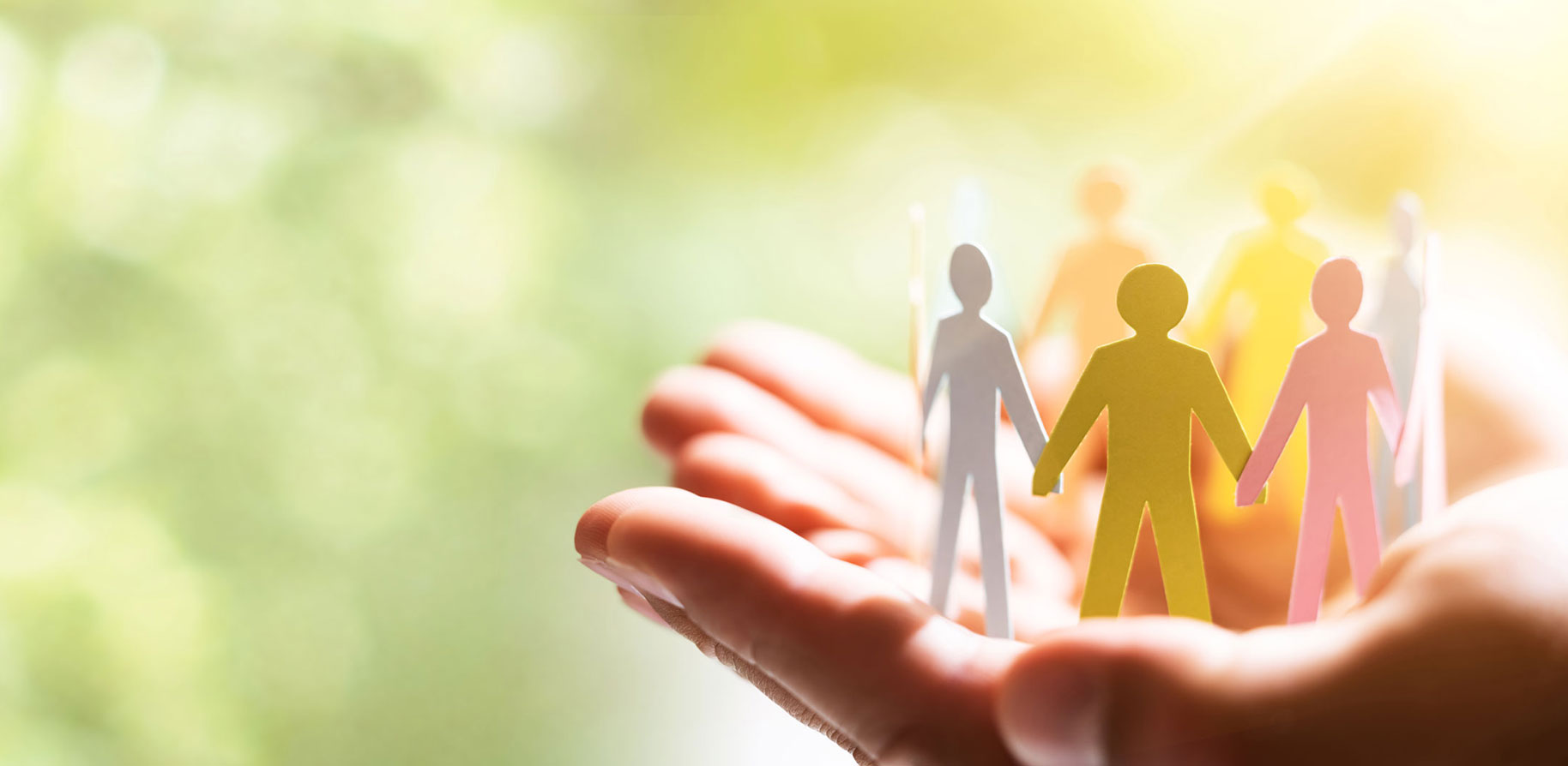 A hand holds paper cutouts of people in various colours, standing together. The background is blurred.